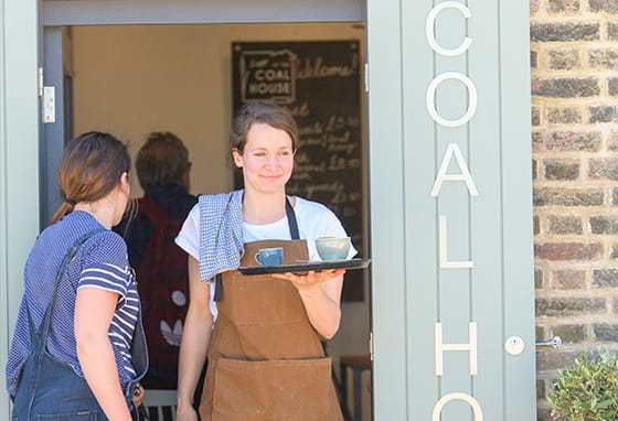 An exterior image of Coal House and someone delivering coffee to a table