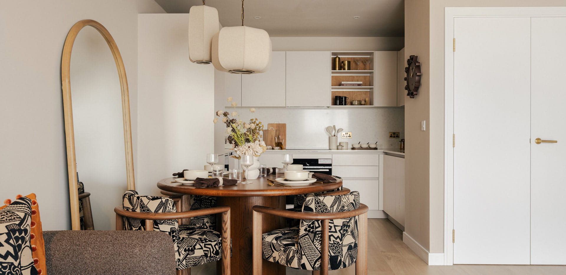 Dining table in foreground, standing mirror behind, kitchenette in background