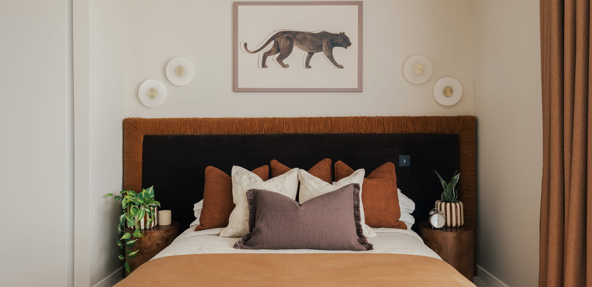 Made-up bed with bedside tables, wall hanging, gold-brown colour curtains