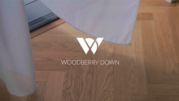 Base of curtains blowing in breeze from open patio doors and view of herringbone wood flooring pattern, Woodberry Down logo shown in centre
