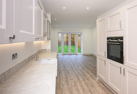 View of an unfurnished kitchen and living room with patio doors in background, design colour is white