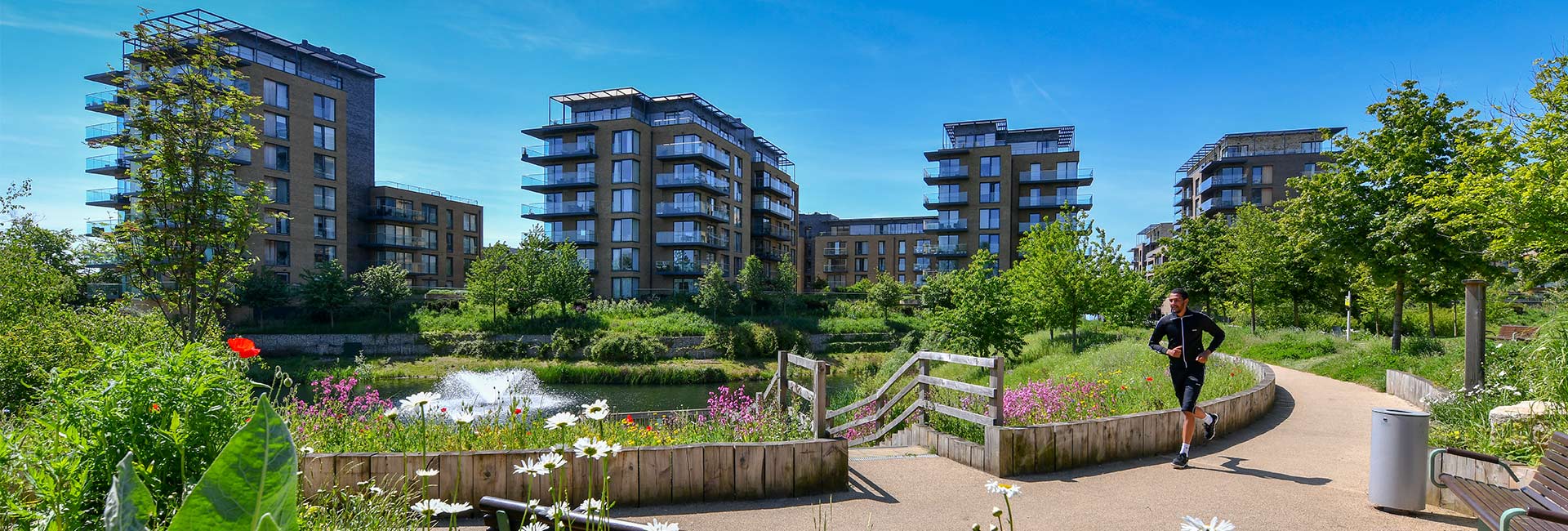 A scenic walkway with landscaping and water body around with new build apartments in background.