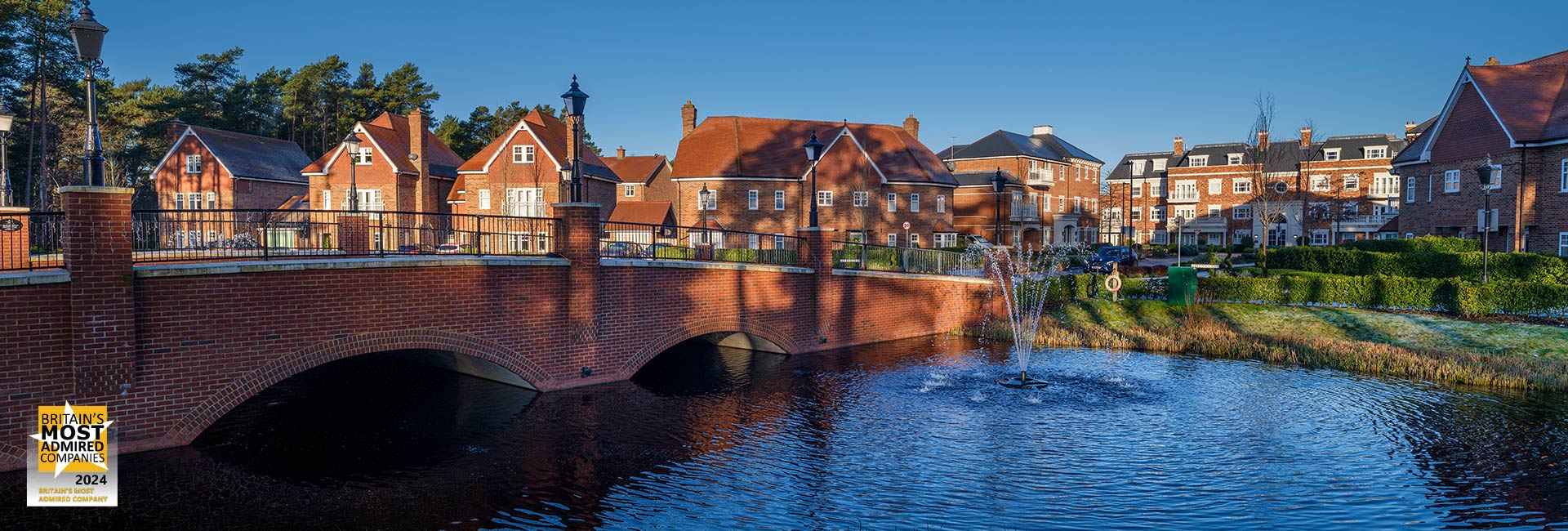 An exterior image of Hartland Village with views of the bridge over the lake into the development
