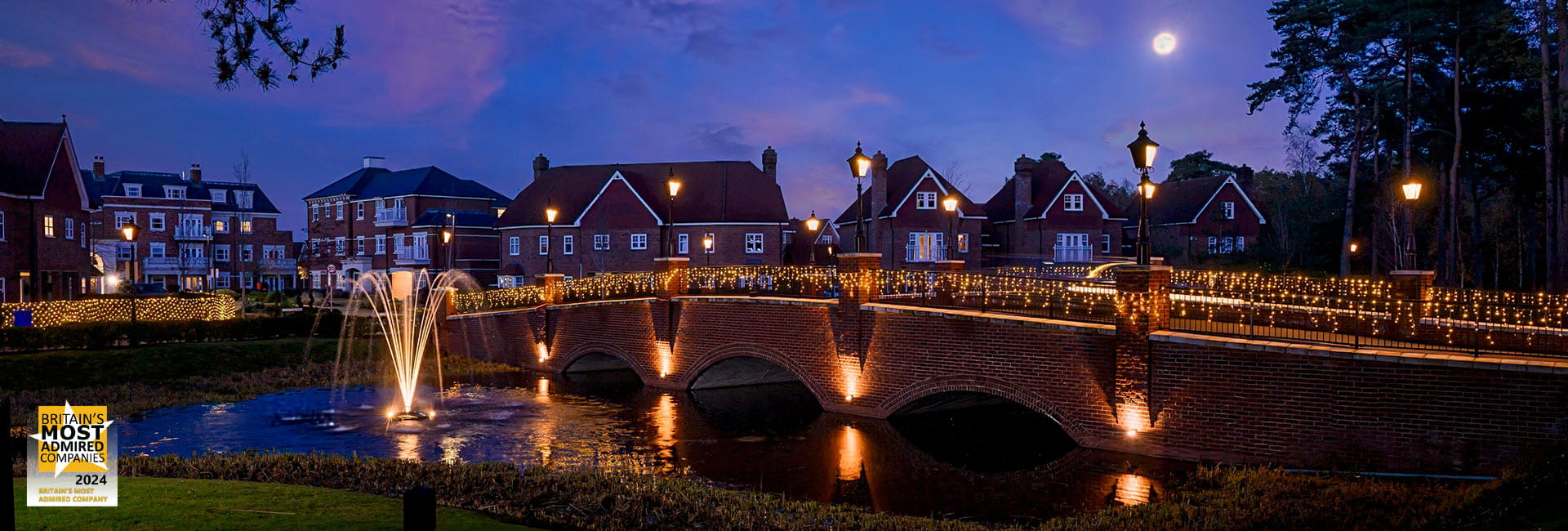 An image of Hartland Village at dusk with beautiful lights on a bridge