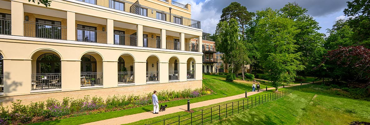An exterior photo of some green space with people walking past a building