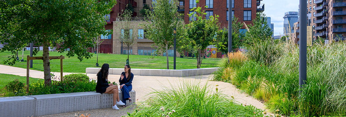 An image of two women sitting on a park wall surrounded by green open space