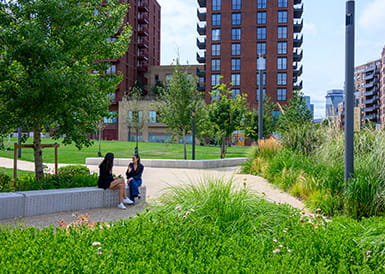 An image of two women sitting on a park wall surrounded by green open space
