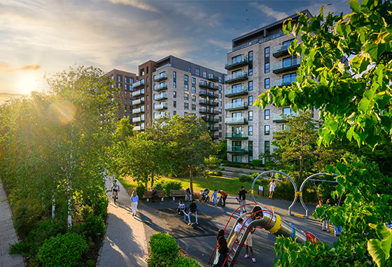 CGI of sunlight streaming through green landscaped playground with new build apartments in background.