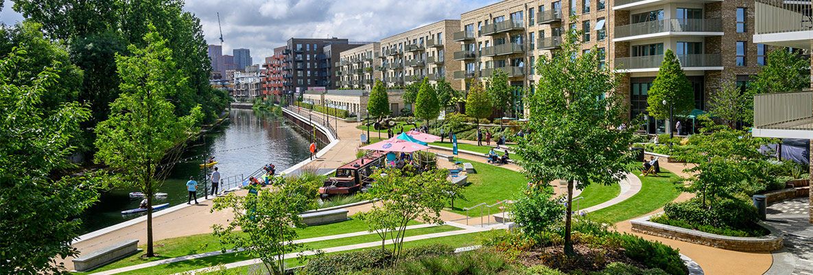 Landscaped greenspaces alongside waterbody with new build developments in background.