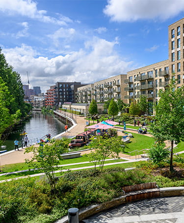 Landscaped greenspaces alongside waterbody with new build developments in background.