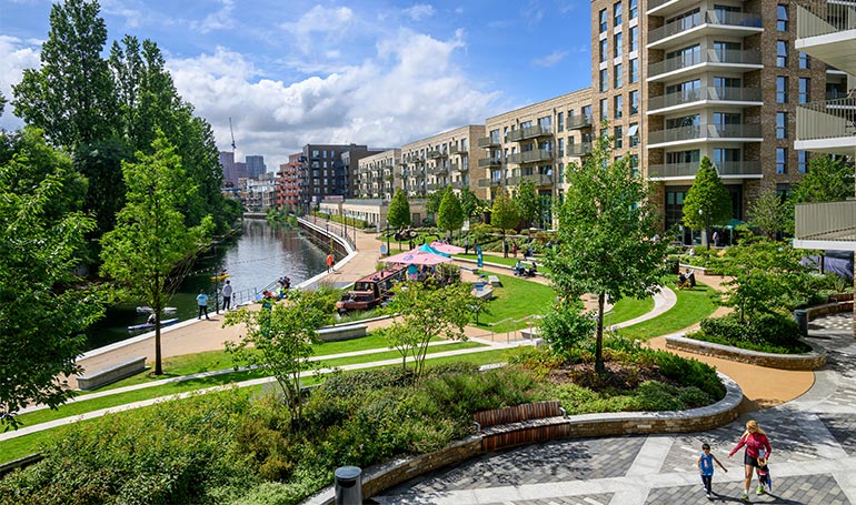Landscaped greenspaces alongside waterbody with new build developments in background.
