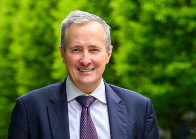 A headshot image of Rob Perrins with greenery in the background